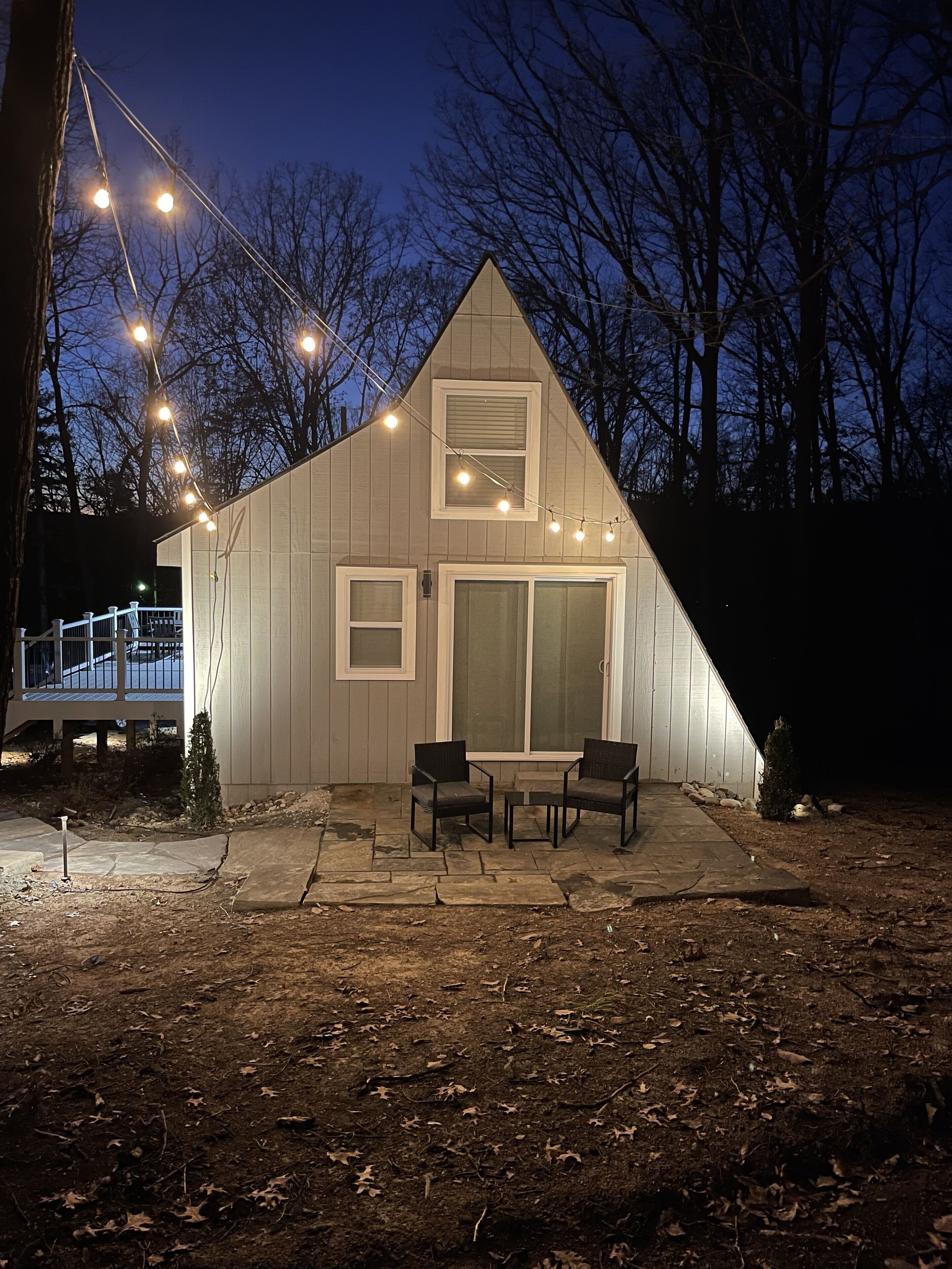 Une maison avec un toit en pente, une grande porte-fenêtre coulissante et une terrasse avec deux chaises et une table.