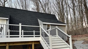 Una casa con fachada blanca, techo gris y una escalera blanca que da a una terraza.