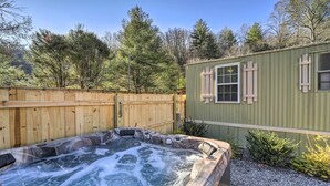 Ein Whirlpool mit einer Holzterrasse, umgeben von einem Holzzaun und einem kleinen Schuppen mit Fenstern.