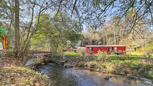 Ein rotes Gebäude mit einer kleinen Brücke über einem Bach, umgeben von Bäumen und Grünpflanzen.