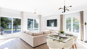 A modern living room with a glass dining table, beige sofa, and large windows offering a view of the outdoors. - Ref. 400719 (Motril)