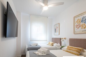 Une chambre d’hôtel avec deux lits, un ventilateur de plafond, un téléviseur à écran plat et des œuvres d’art accrochées aux murs.