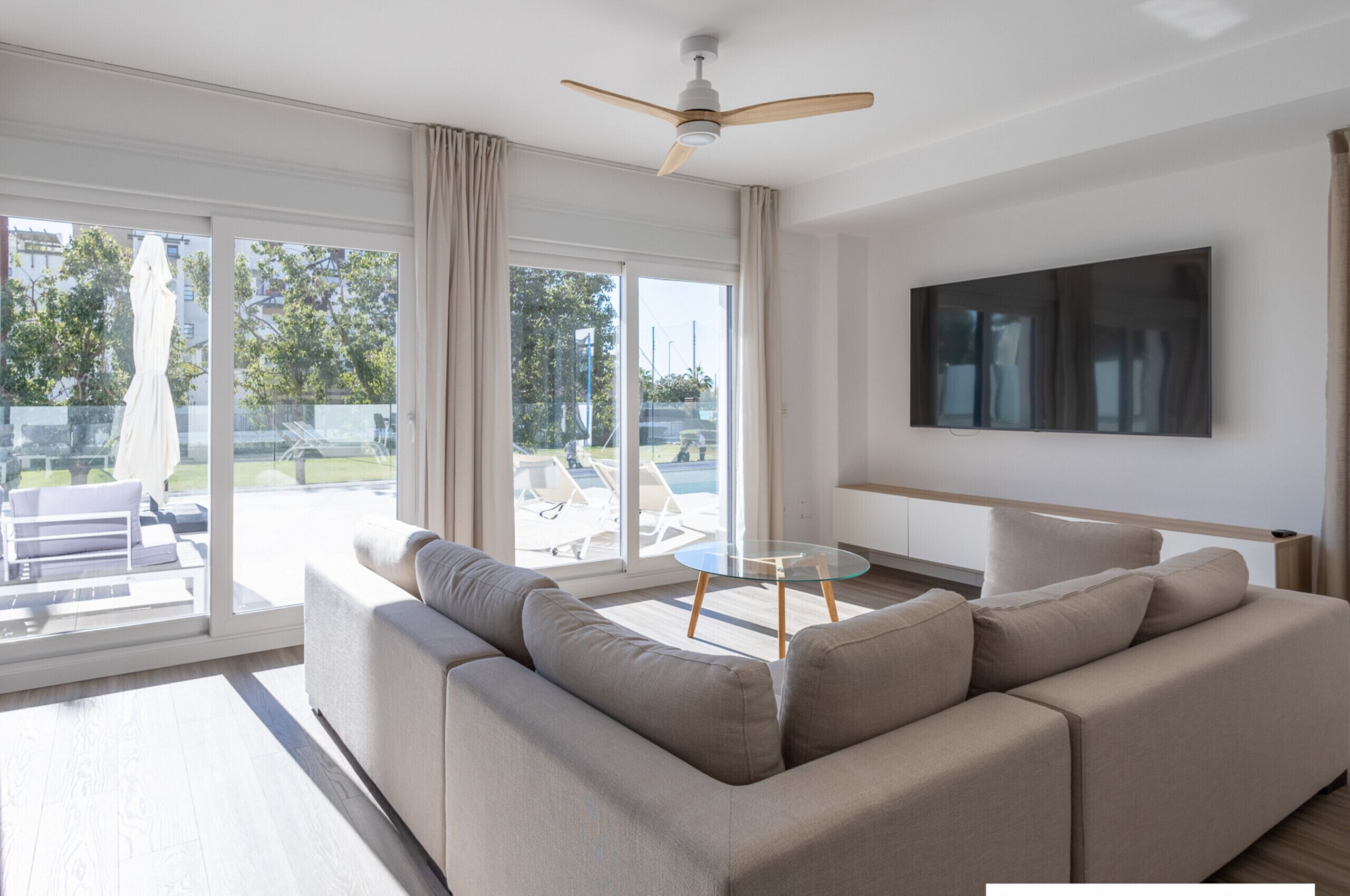 Een moderne woonkamer met een beige bank, een glazen salontafel en een plafondventilator.