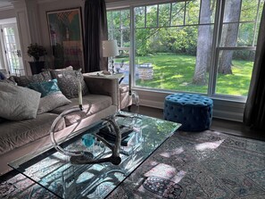 A living room with a sofa, a glass coffee table, and a view of a green garden through large windows. - Lake Forest Luxury 4 Bedroom Monthly Stays Executive Housing (Lake Forest)