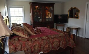A bedroom with a large bed, a wooden cabinet, a television, and a mirror.