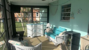 Una habitación iluminada por el sol con muebles de mimbre, un armario blanco y un sofá color turquesa.