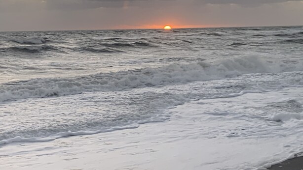 Una playa con olas y un atardecer.