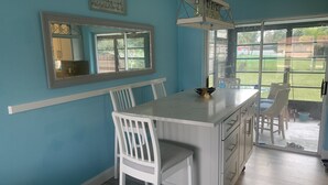 Una cocina con una isla blanca, sillas blancas, un ventanal y vistas al exterior.