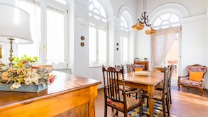 A dining area with a wooden table and chairs, a chandelier, and a view of the outside through large windows.