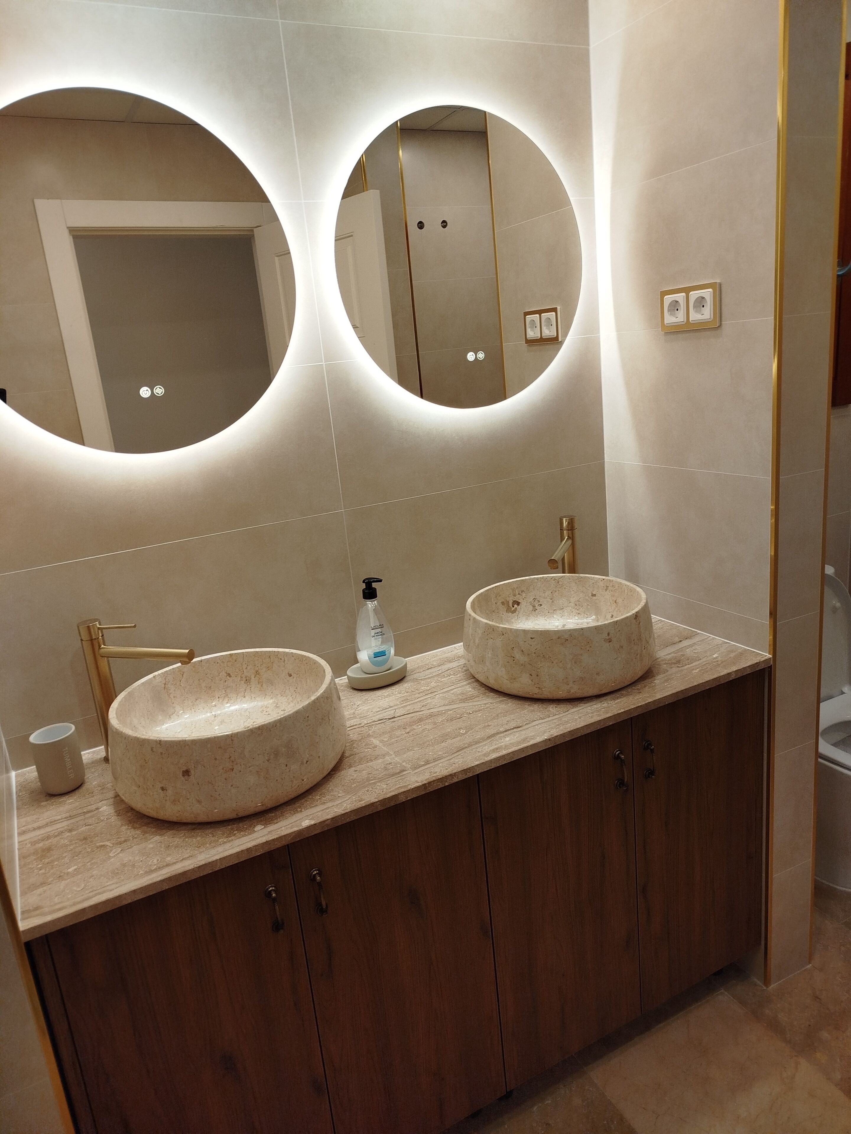 A bathroom with two round sinks, a mirror, and a toilet.