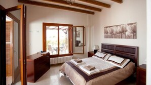 A bedroom with a large bed, wooden ceiling beams, a sliding glass door to a patio, and a framed floral artwork on the wall.