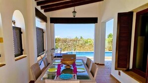 A dining area with a table set for four, a wicker chair, and a view of the sea.