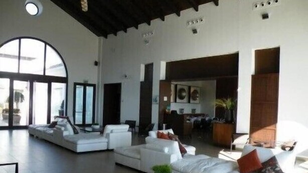 A spacious living area with a large sofa set, a coffee table, and a dining area in the background.