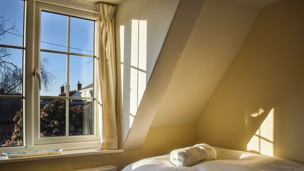 Una camera da letto con un letto singolo, una finestra con tende e un termosifone.