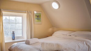 Una camera da letto con un letto grande, una finestra con tende, un quadro appeso al muro e un comodino.