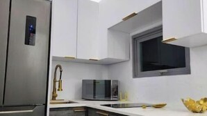 Una cocina moderna con microondas integrado, refrigerador de acero inoxidable y una ventana sobre el fregadero.