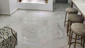 Una cocina moderna con televisor empotrado, suelo de mármol y taburetes de bar.