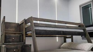 Una cama litera con escalones de madera y cajones, paredes blancas y una ventana.