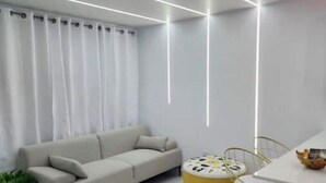 Ein modernes Wohnzimmer mit einer Couch, einem runden, gelben Ottomanen und einem Essbereich mit Tisch und Stühlen.