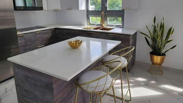 Una cocina moderna con una isla central, taburetes de bar, una planta en maceta y una ventana con vistas a zonas verdes.
