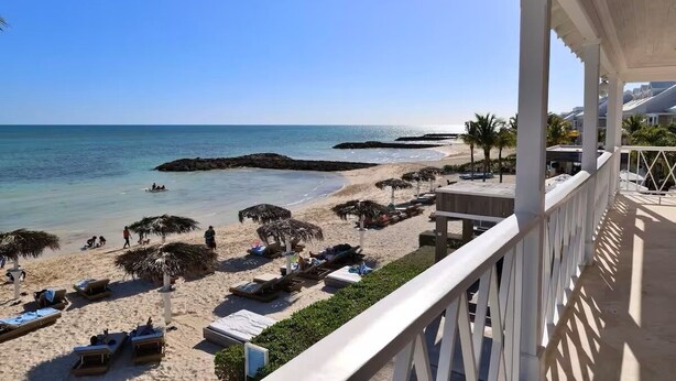 Blick auf einen Strand von einem Balkon mit Liegestühlen, Sonnenschirmen und blauem Himmel.