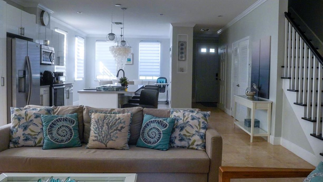 A modern living room with a beige sofa, a glass coffee table, and a kitchen in the background.