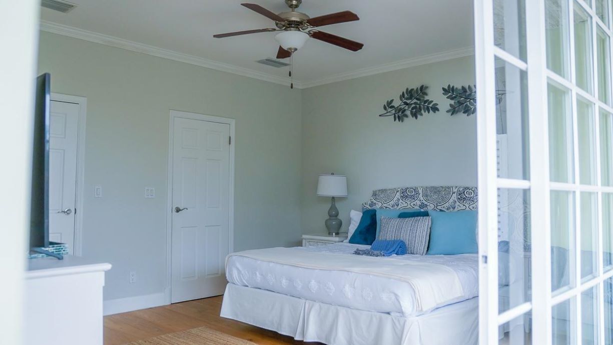 A bedroom with a bed, a nightstand, a ceiling fan, and a door.