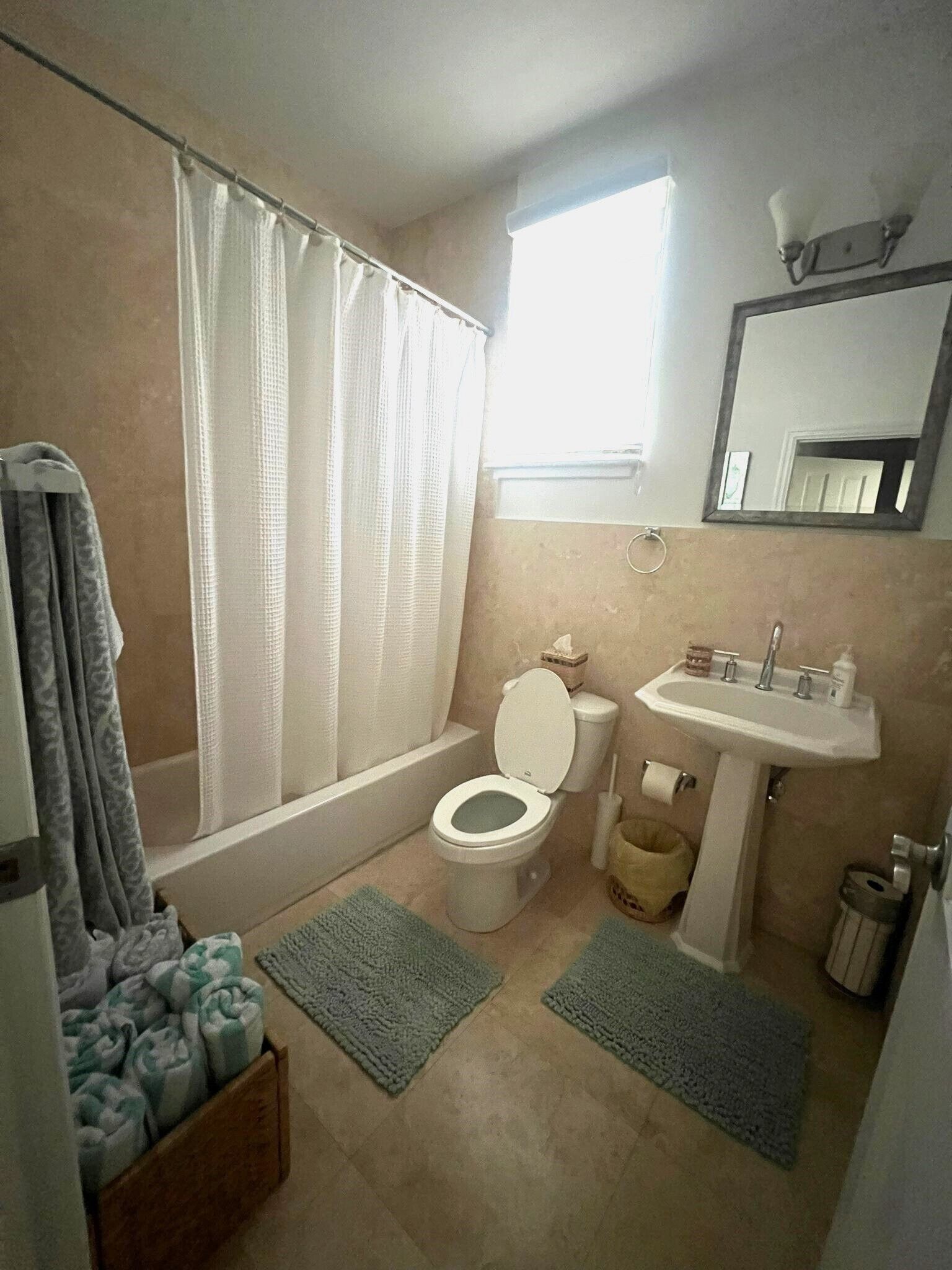 Un baño con inodoro, lavabo y bañera. Hay dos alfombras en el suelo.
