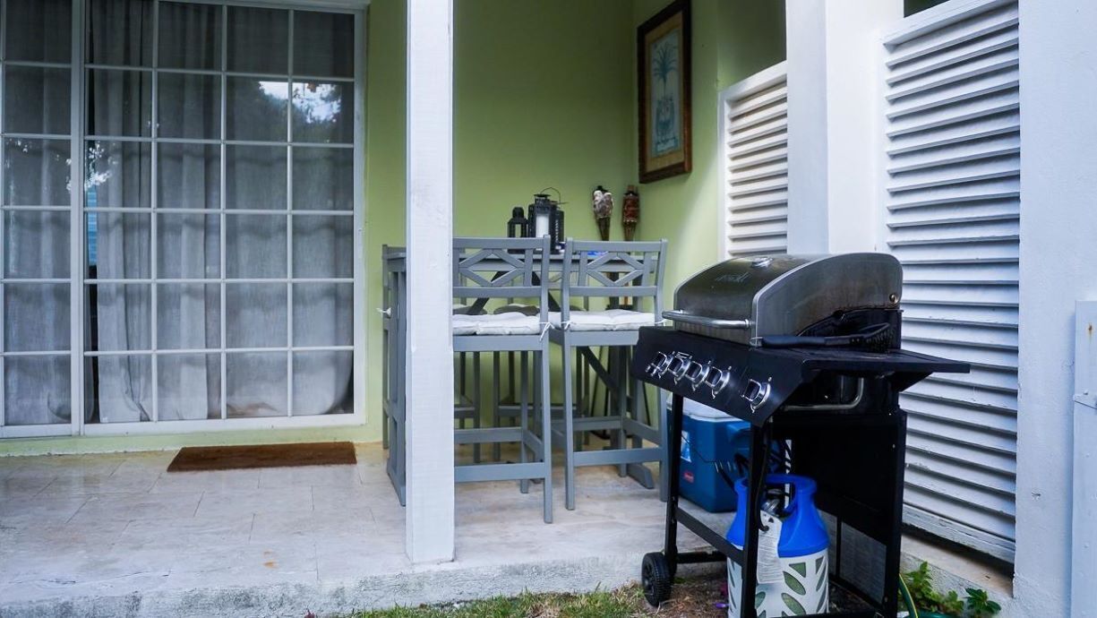 An outdoor patio with a grill, a dining table with chairs, and a blue cooler.