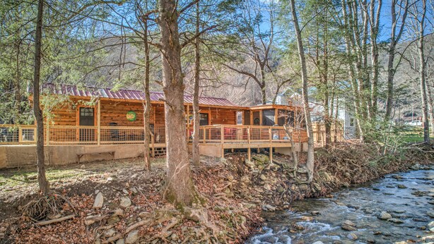 Une cabane rustique avec un toit en métal, une terrasse en bois et une rivière qui coule à proximité.