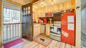Une cuisine de taille réduite, avec des meubles de rangement en bois, un réfrigérateur rouge, un four à micro-ondes et une cuisinière.