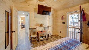 Une pièce de cabane en bois comprenant un lit, deux chaises, une table, un téléviseur et une porte donnant sur l’extérieur.