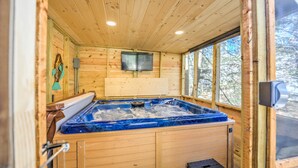 L’intérieur d’un chalet en bois est doté d’un bain à remous, de murs en bois, d’un téléviseur fixé au mur et d’une fenêtre donnant sur la forêt.