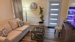 A living room with a beige sofa, a glass coffee table, a potted plant, and a television on a wooden stand. - Cute, clean and cozy cottage. 5 minute drive from Junkanoo beach and Bay street. (Nassau)
