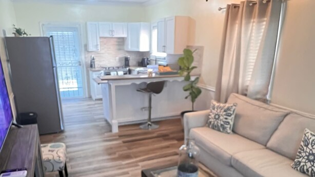 A living room with a sofa, coffee table, and a TV. There is a kitchen in the background with white cabinets and a dining area. - Cute, clean and cozy cottage. 5 minute drive from Junkanoo beach and Bay street. (Nassau)