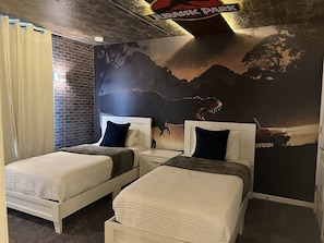 Una habitación con dos camas, una pared de ladrillo y un mural de un dinosaurio.