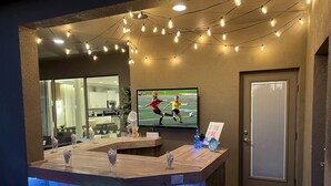 Un'area bar con un bancone, sgabelli, una TV che trasmette un evento sportivo e luci decorative a stringa.