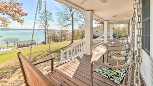 A covered porch with a swing, a view of the lake, and a dining area with outdoor furniture. - Country-Chic Home w/ Fire Pit, Steps to Lake! (New Concord)