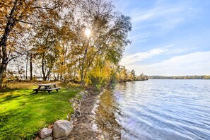Zona de picnic junto al lago con banco y mesa, rodeada de árboles y una vista despejada del agua.