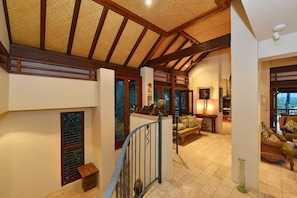 A spacious interior with a high ceiling, wooden beams, a staircase, and a seating area with a view.