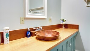 A bathroom with a wooden vanity, a large mirror, a wooden bowl sink, and toiletries on the counter. - All-Season Ludlow Apartment: 3 Mi to Okemo Resort! (Ludlow)