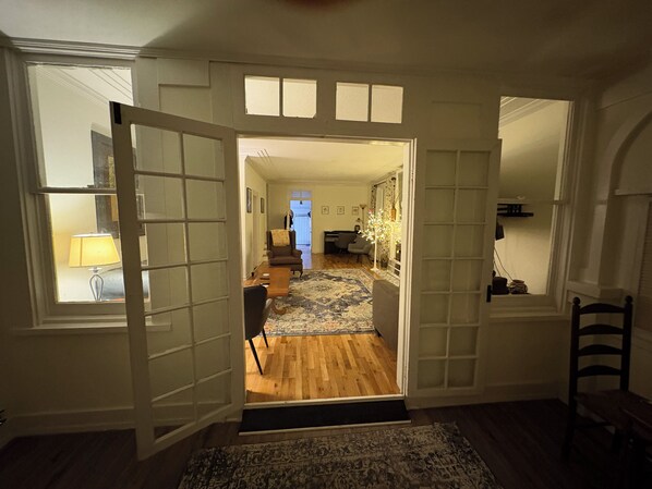 Una puerta abierta que da a una sala de estar con piso de madera, un tapete estampado y un comedor con mesa y sillas.