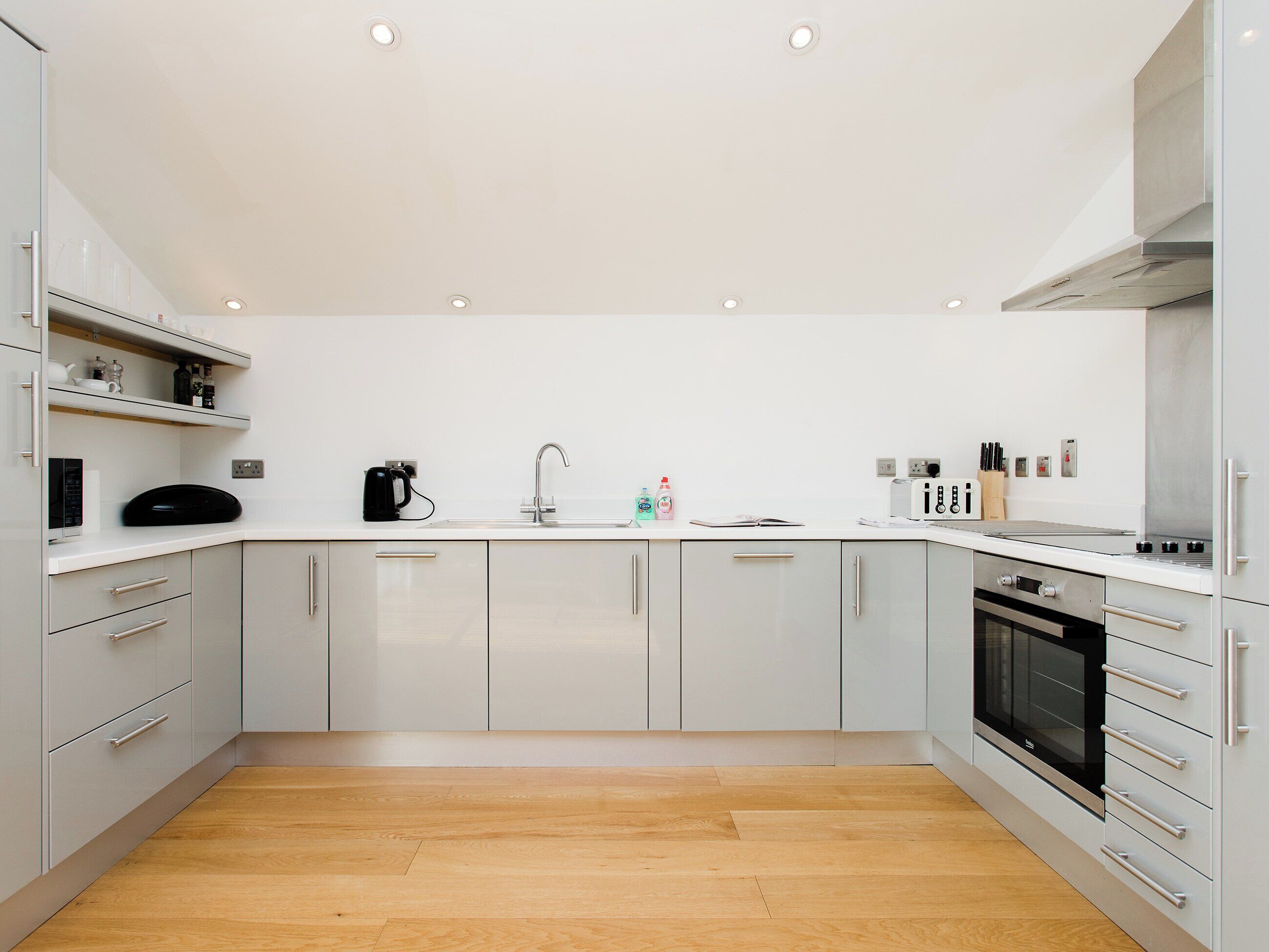 A modern kitchen with white cabinets, a stainless steel sink, and a built-in oven.