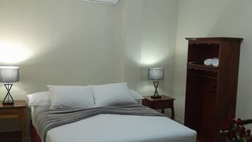 A bedroom with a bed, two bedside tables with lamps, a ceiling fan, an air conditioning unit, and a wooden wardrobe.