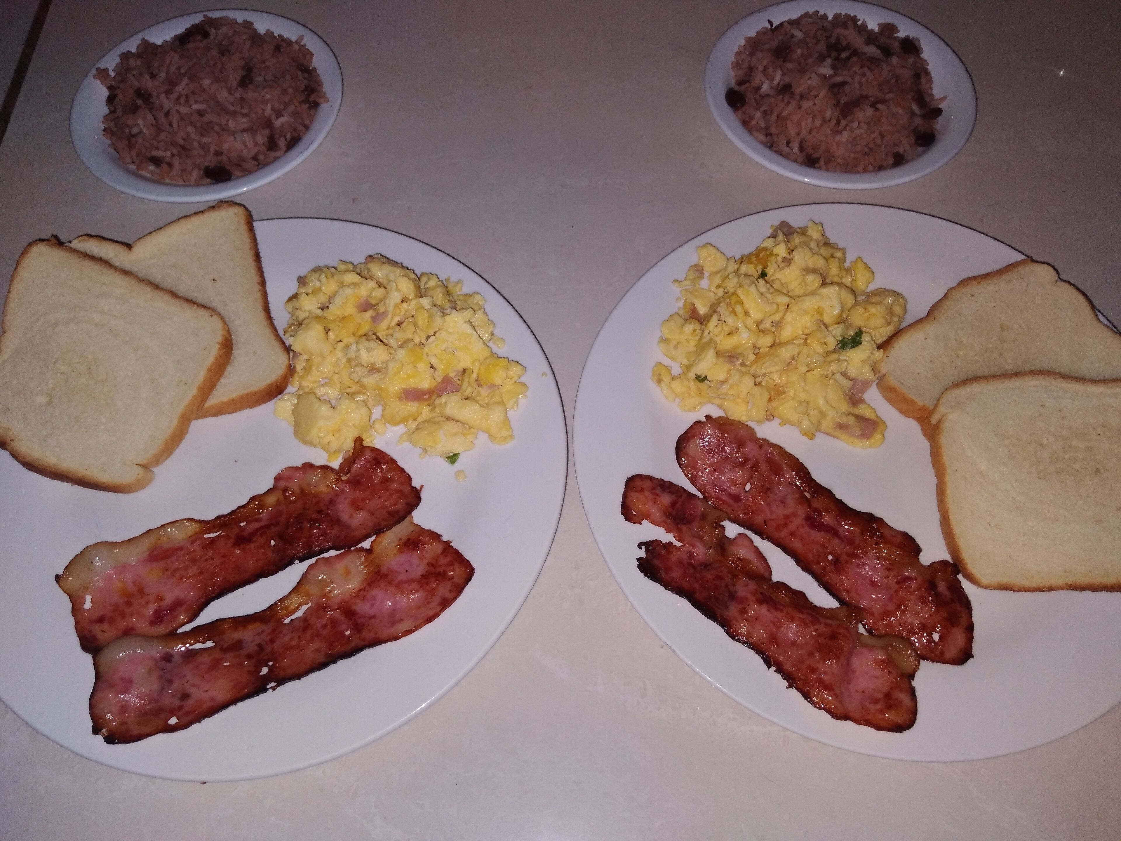 Two plates with scrambled eggs, bacon, toast, and beans.