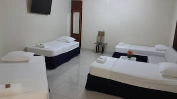 Quarto de hotel com duas camas de solteiro, um sofá-cama, uma TV, um ventilador de teto e uma pequena mesa com abajur.