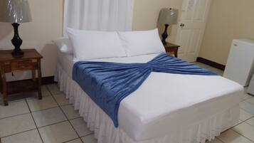 A neatly made bed with a blue blanket, two bedside tables with lamps, a white door, and a white radiator.