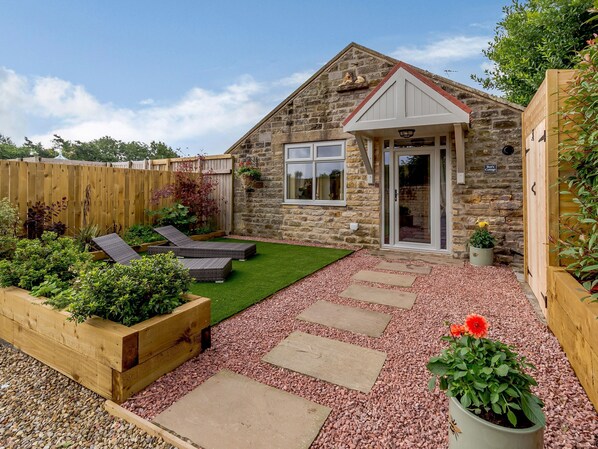 A stone cottage with a small garden, a wooden fence, and a paved patio area.