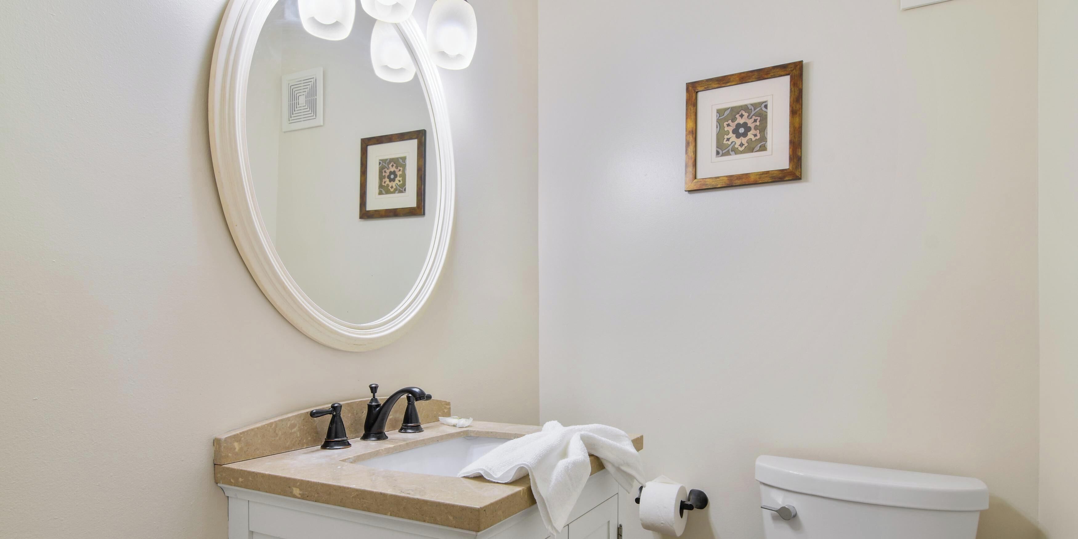 Ein Badezimmer mit Waschbecken, Spiegel, Toilette und gerahmten Bildern an der Wand.