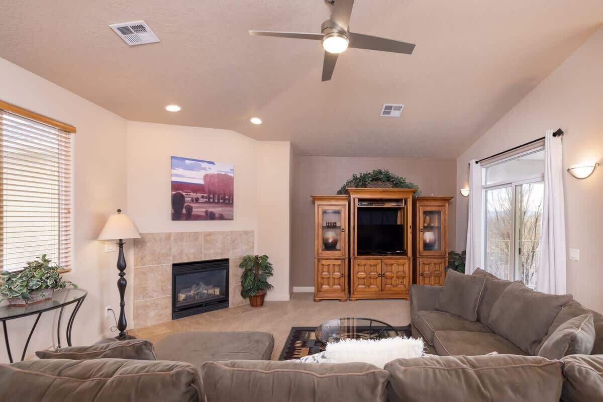 A living room with a fireplace, a ceiling fan, and a large window.